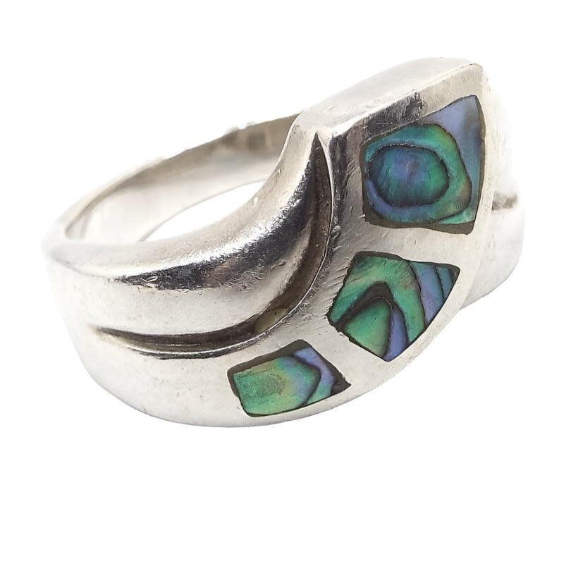 Angled front view of the retro vintage sterling silver abalone ring. It has a curved bypass design at the top with three pieces of inlaid pearly multi color abalone shell. 