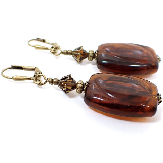 Side view of the handmade faux tortoise drop earrings. The metal is antiqued brass in color. There are faceted brown glass crystals at the top. The bottom beads are rectangle in shape with rounded edges and have an imitation tortoise design of marbled brown and black colors. 