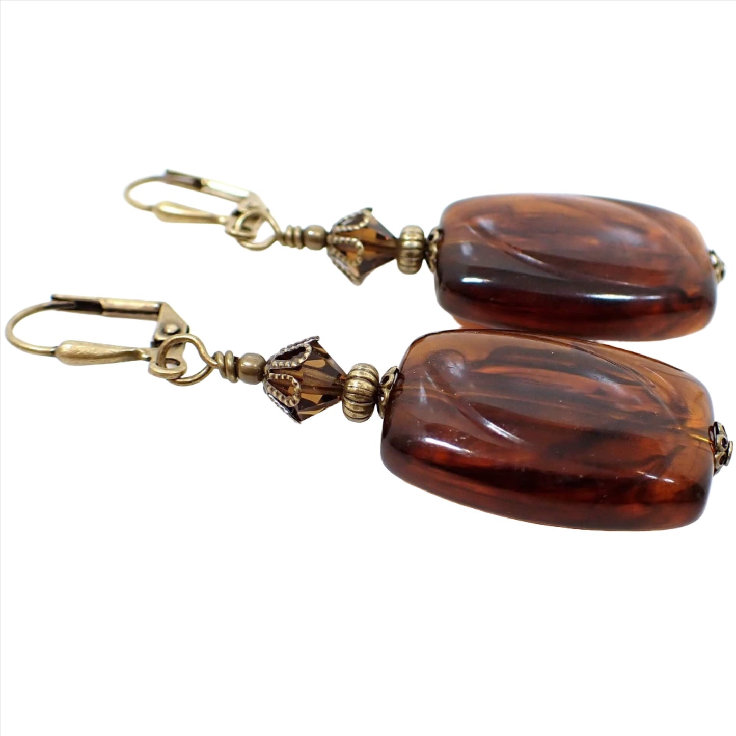 Side view of the handmade faux tortoise drop earrings. The metal is antiqued brass in color. There are faceted brown glass crystals at the top. The bottom beads are rectangle in shape with rounded edges and have an imitation tortoise design of marbled brown and black colors. 