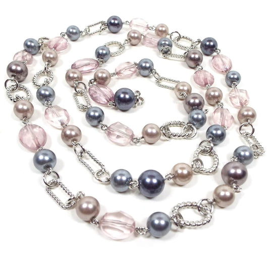 Front view of the retro vintage Premier Designs beaded necklace. The necklace is beaded with faux pearls in shades of pink, purple, and gray, as well as faceted pink plastic beads. There are silver tone oval links in between some of the beads throughout the necklace.