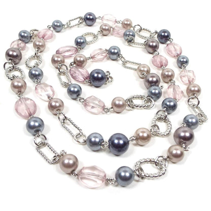 Front view of the retro vintage Premier Designs beaded necklace. The necklace is beaded with faux pearls in shades of pink, purple, and gray, as well as faceted pink plastic beads. There are silver tone oval links in between some of the beads throughout the necklace.