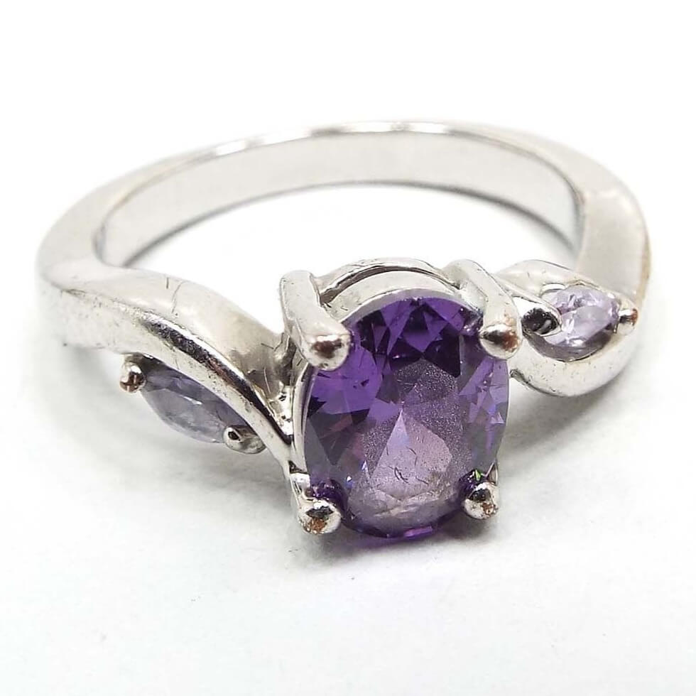 Front view of the retro vintage rhinestone cocktail ring. The metal is silver tone in color. There is a purple oval rhinestone on the top and a marquis clear rhinestone on each side. All stones are prong set.