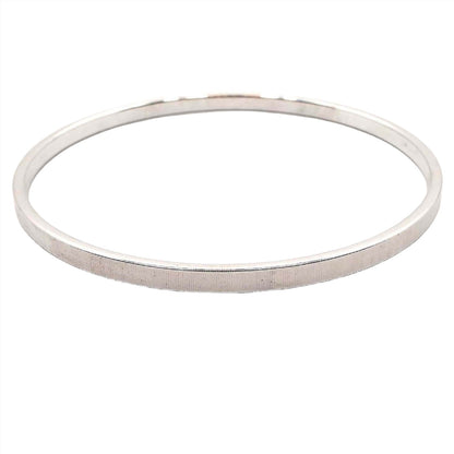 Angled side view of the retro vintage Monet stacking bangle bracelet. It is silver tone in color and is thinner in width. The outside edge has a textured design made up of tiny lines.