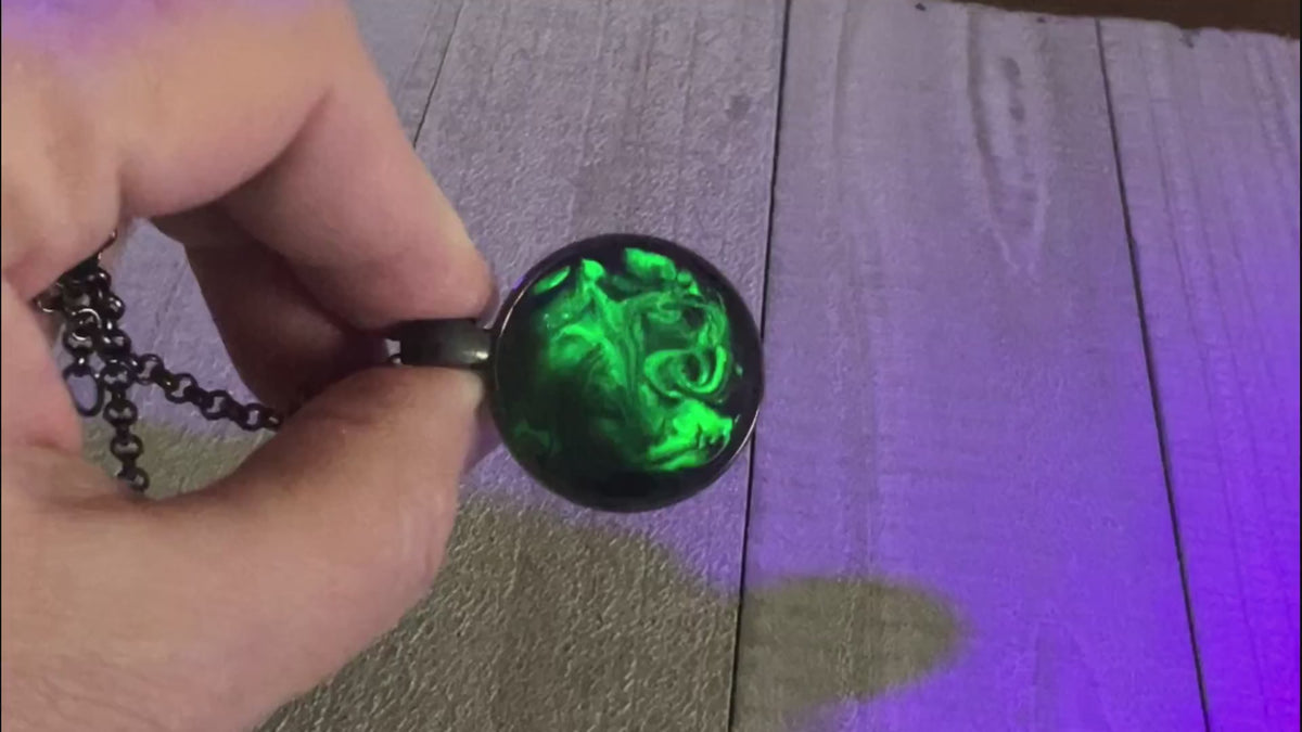 Video showing the handmade black and neon green resin necklace pendant fluorescing under a UV black light. 