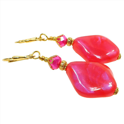 Angled side view of the handmade color shift earrings. The metal is gold plated in color. There are hot pink faceted glass crystals at the top. The bottom beads are shaped like curved and angled teardrops are are bright pink lucite with shimmers of purple color as you move around in the light.