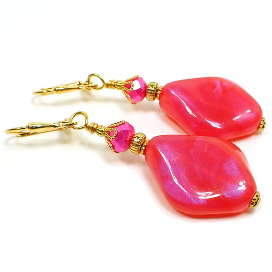 Angled side view of the handmade color shift earrings. The metal is gold plated in color. There are hot pink faceted glass crystals at the top. The bottom beads are shaped like curved and angled teardrops are are bright pink lucite with shimmers of purple color as you move around in the light.