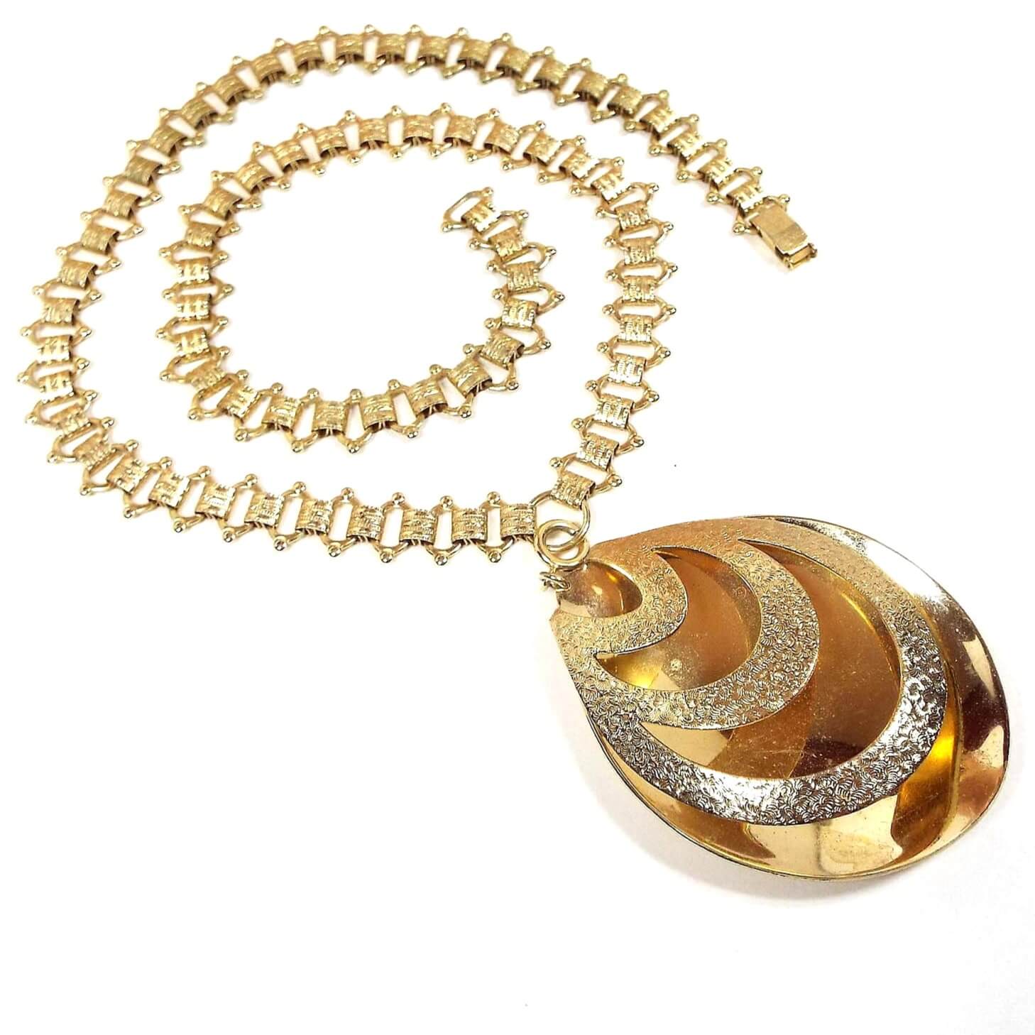 Top view of the Mid Century Vintage Sarah Coventry large teardrop pendant necklace. The chain is gold tone with fancy open links and textured pattern links. There is a snap lock clasp on the end. The pendant is a large teardrop with a cut areas on the front and a spring ring clasp at the top so you can remove it from the chain if you want.