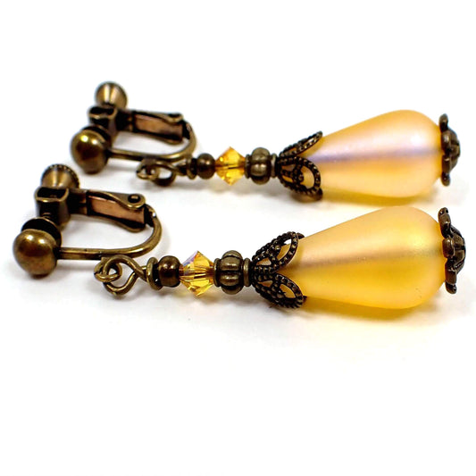 Side view of the handmade yellow teardrop earrings. The metal is antiqued brass in color. The top beads are small faceted glass dark yellow beads and the bottom beads are a frosted rich yellow lucite teardrop bead. 