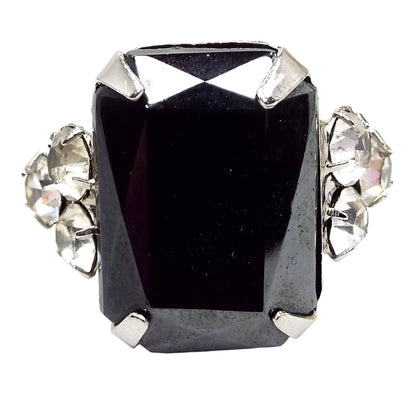 Front view of the Mid Century vintage adjustable rhinestone ring. The metal is silver tone in color. There is a large rectangle shaped imitation hematite rhinestone on the front with a cluster of three smaller round clear rhinestones on each side.