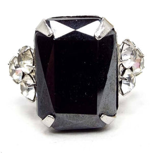 Front view of the Mid Century vintage adjustable rhinestone ring. The metal is silver tone in color. There is a large rectangle shaped imitation hematite rhinestone on the front with a cluster of three smaller round clear rhinestones on each side.