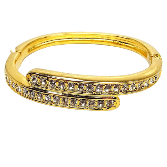Front view of the retro vintage rhinestone bangle bracelet. It is gold tone in color. The top part has two curved bar areas that have a bypass style design. Each has a row of round clear rhinestones on it. The bottom of the bangle is plain metal.