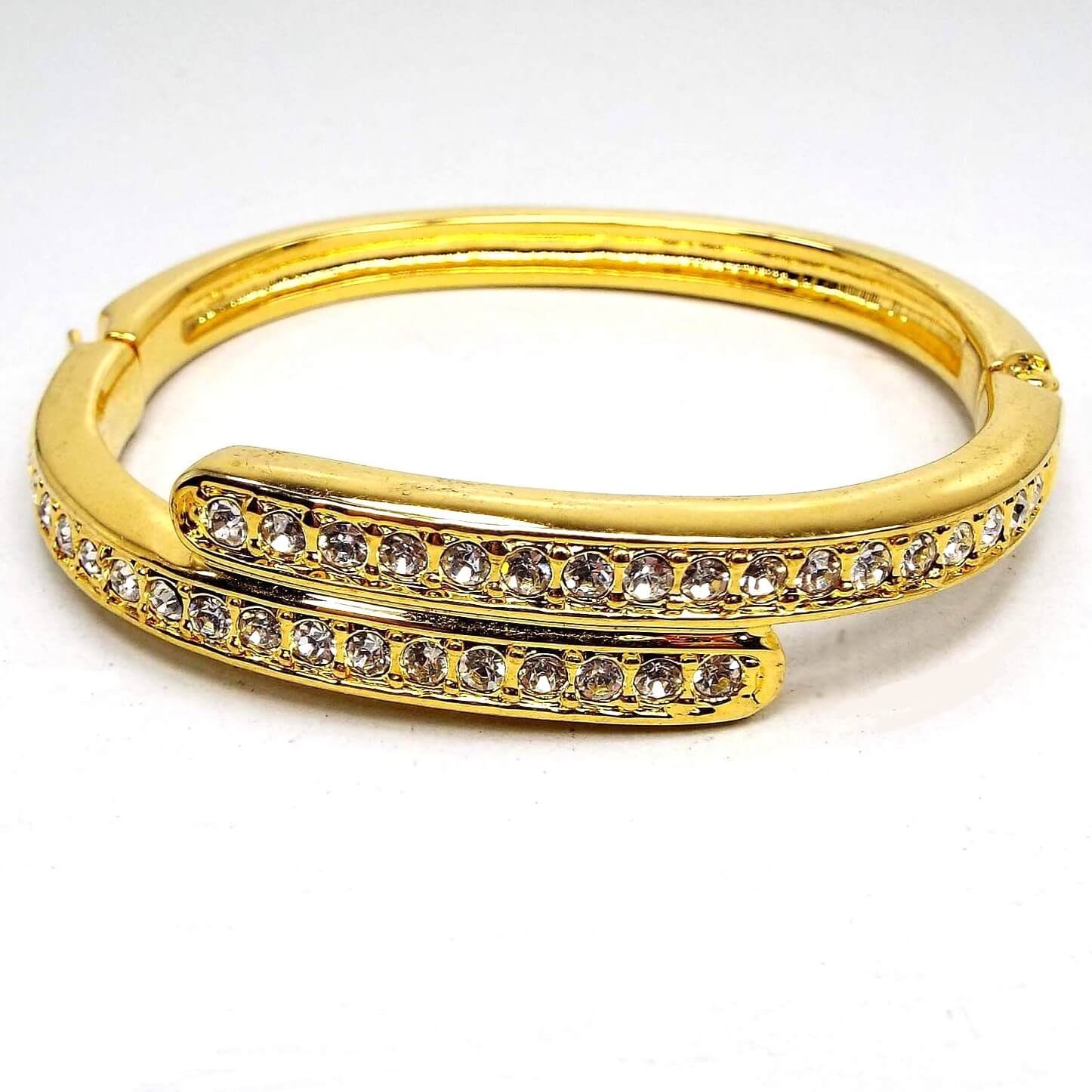 Front view of the retro vintage rhinestone bangle bracelet. It is gold tone in color. The top part has two curved bar areas that have a bypass style design. Each has a row of round clear rhinestones on it. The bottom of the bangle is plain metal.