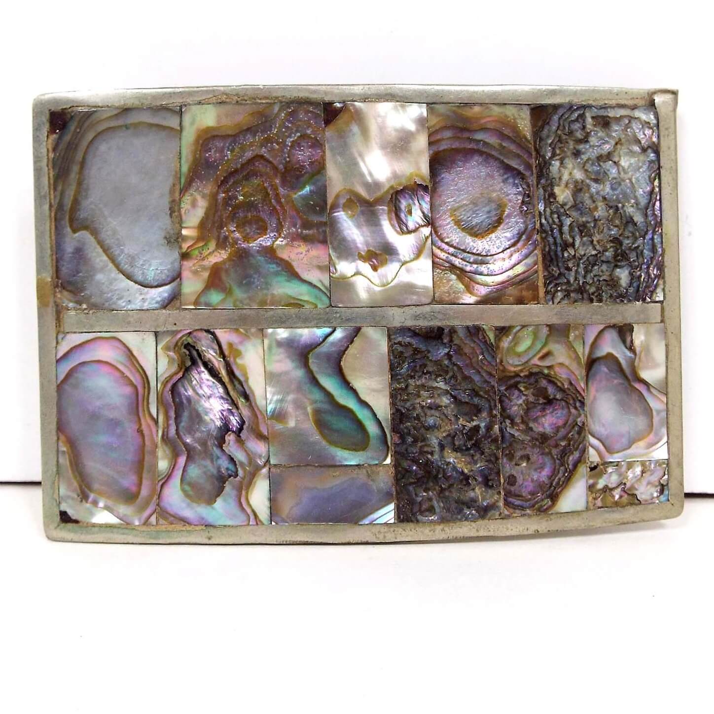Front view of the retro vintage abalone belt buckle made in Mexico. It is rectangle in shape with silver tone color metal. There are rectangular pieces of abalone shell inlaid across two rows on the front.