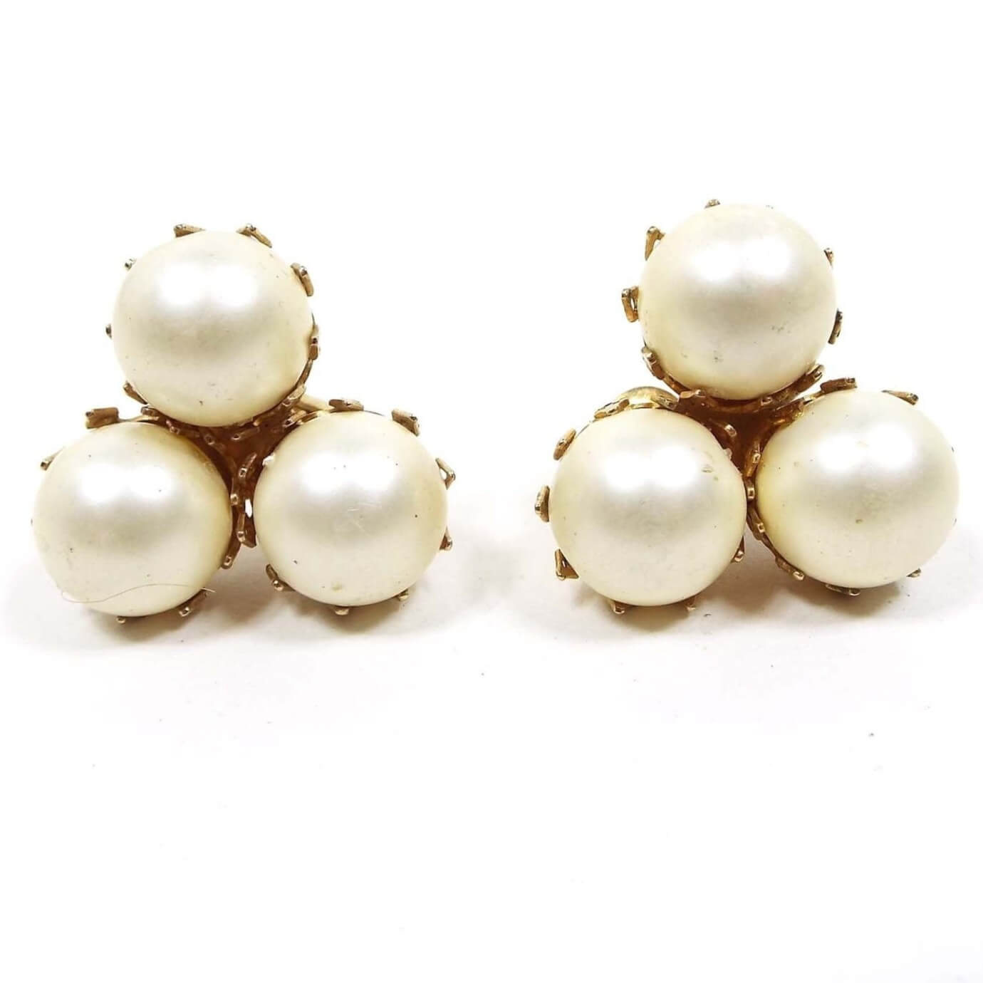 Front view of the Mid Century vintage Castlecliff clip on earrings. There are three round off white pearls in gold tone color prong settings.