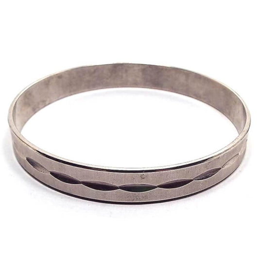 Angled view of the Mid Century vintage textured bangle bracelet. It is darkened silver tone in color and has a tiny ridged line design. There are cut oval shapes all the way around the middle of the bracelet.