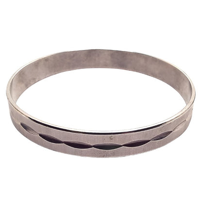 Angled view of the Mid Century vintage textured bangle bracelet. It is darkened silver tone in color and has a tiny ridged line design. There are cut oval shapes all the way around the middle of the bracelet.