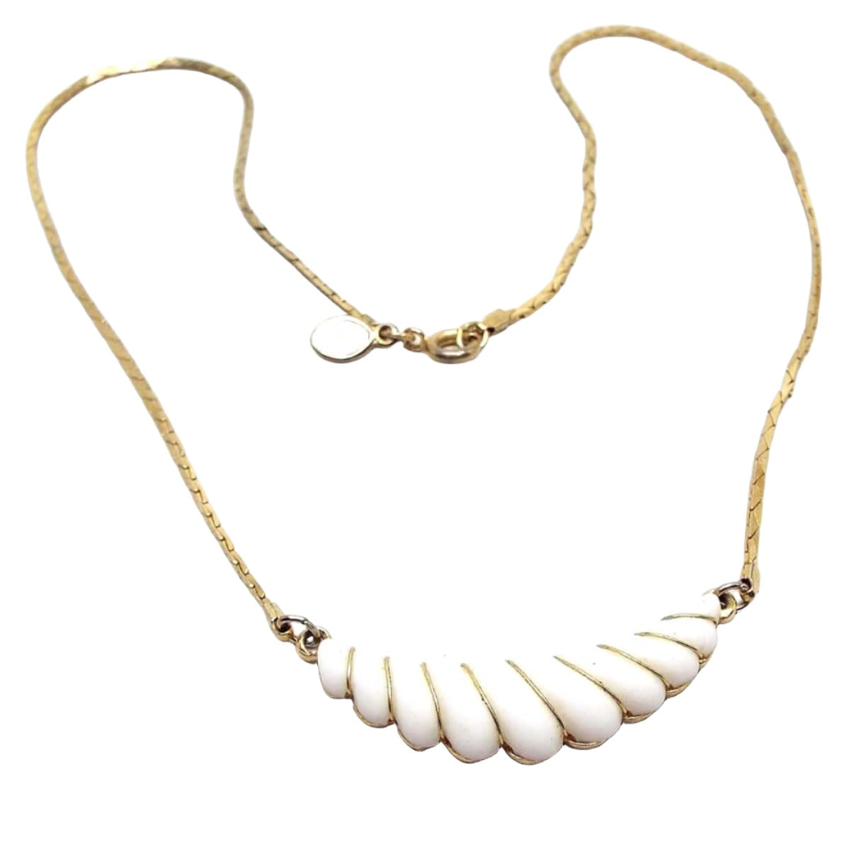 Front view of the retro vintage Avon pendant necklace. The metal is gold tone in color. The bottom pendant area is curved on top and scalloped on the bottom. There is a white plastic front with gold tone wire wrapping in between each scalloped area. 