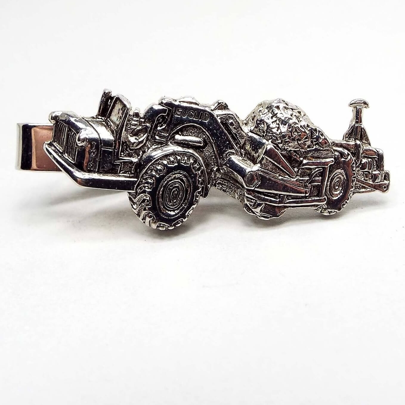Front view of the retro vintage Euclid Twin Engine Scraper tie clip. The metal is silver tone in color. It has a detailed design the of the piece of road construction equipment.