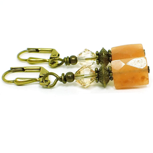 Angled view of the handmade peach aventurine earrings. The metal is antiqued brass. There are faceted glass crystal beads in light peach at the top. The bottom gemstone beads are faceted rectangles with shades of peach.