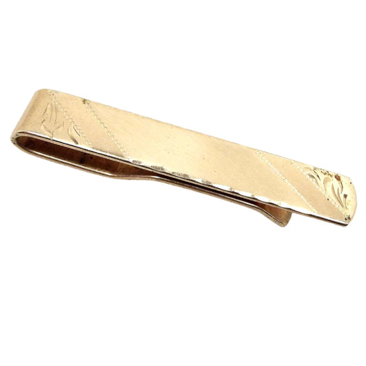 Angled front view of the Mid Century vintage etched tie bar. The metal is gold tone in color. There are diagonal areas of matte and shiny gold tone. At each end is an etched leaf like design. The bottom and top edge have a beveled texture.