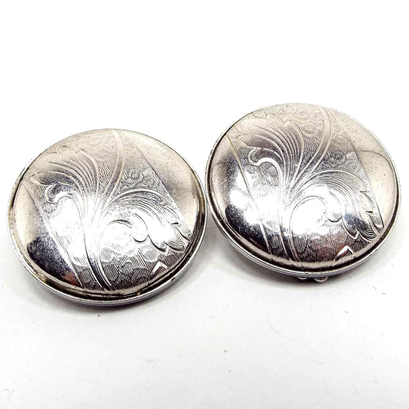 Front view of the Mid Century vintage clip on earrings. They are round and silver tone in color. There is a stamped area across the middle that has a leaf like textured design on it.