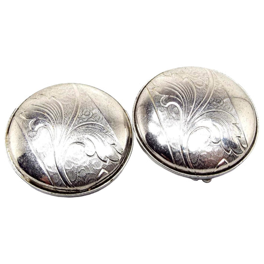 Front view of the Mid Century vintage clip on earrings. They are round and silver tone in color. There is a stamped area across the middle that has a leaf like textured design on it.