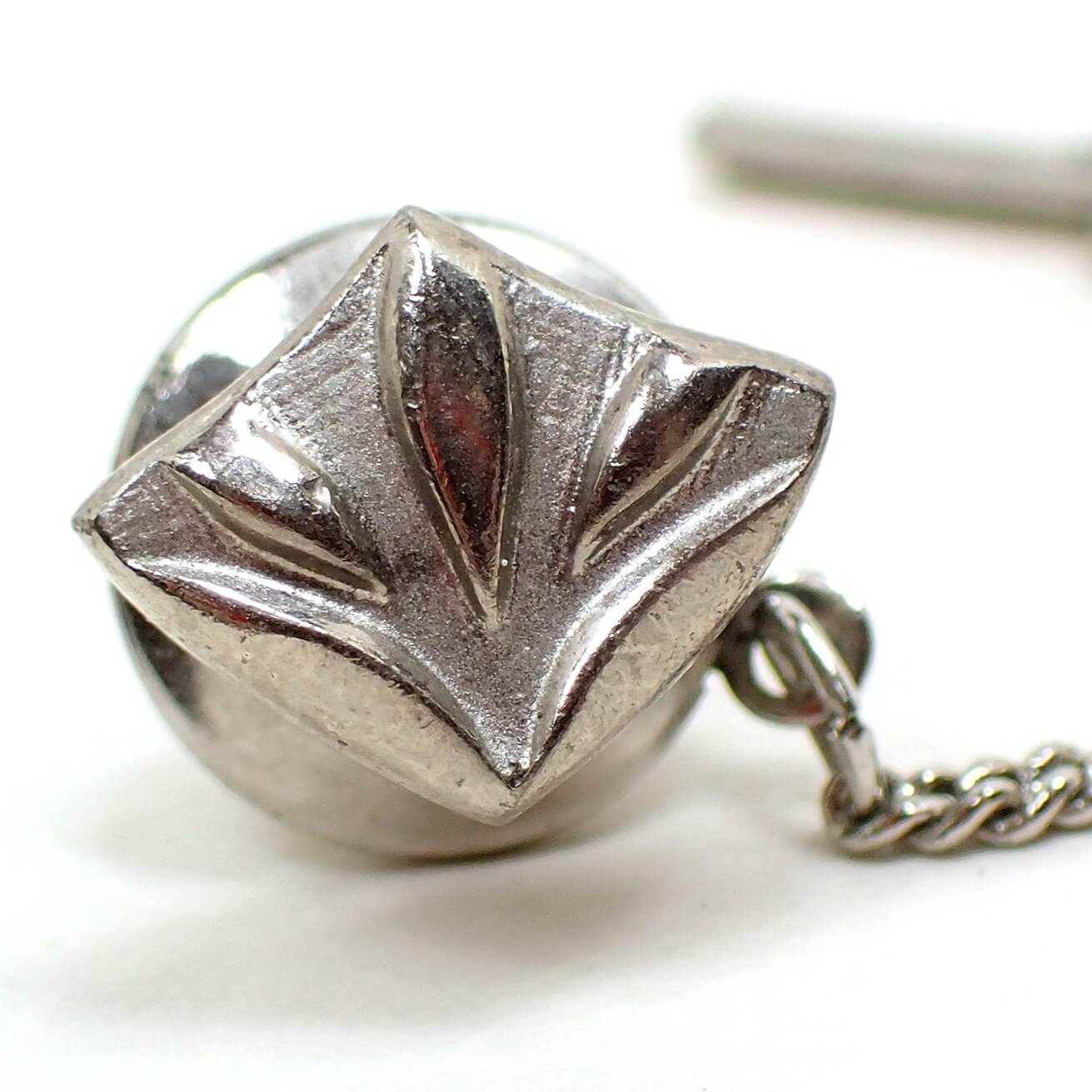Front view of the Mid Century vintage Modernist style tie tack. It is silver tone in color. It has a point towards the bottom and the top flares out with a leaf like design.