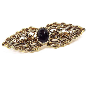 Front view of the Victorian Revival retro vintage brooch pin. The metal is antiqued gold tone in color. The brooch has a filigree design the a teardrop shape on each side with the points going outwards. There is an oval in the middle with a domed black glass cab.