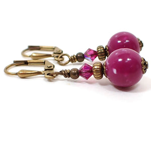 Side view of the handmade drop earrings with vintage lucite beads. The metal is antiqued brass in color. The top faceted glass crystal beads are a bright fuchsia pink purple in color. The bottom lucite beads are fuchsia in color also and have specks of white marbled in here and there. 