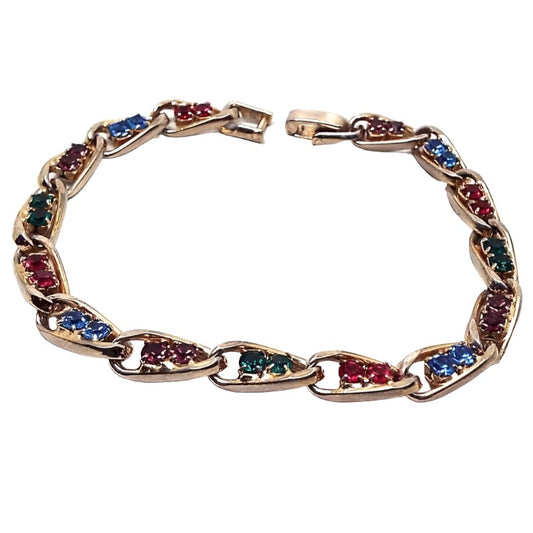 Top view of the Mid Century vintage rhinestone bracelet. The metal is gold tone in color. The links are twisted oval shape and each link has two rhinestones. The colors alternate between the links of red, blue, green, and purple rhinestones. 
