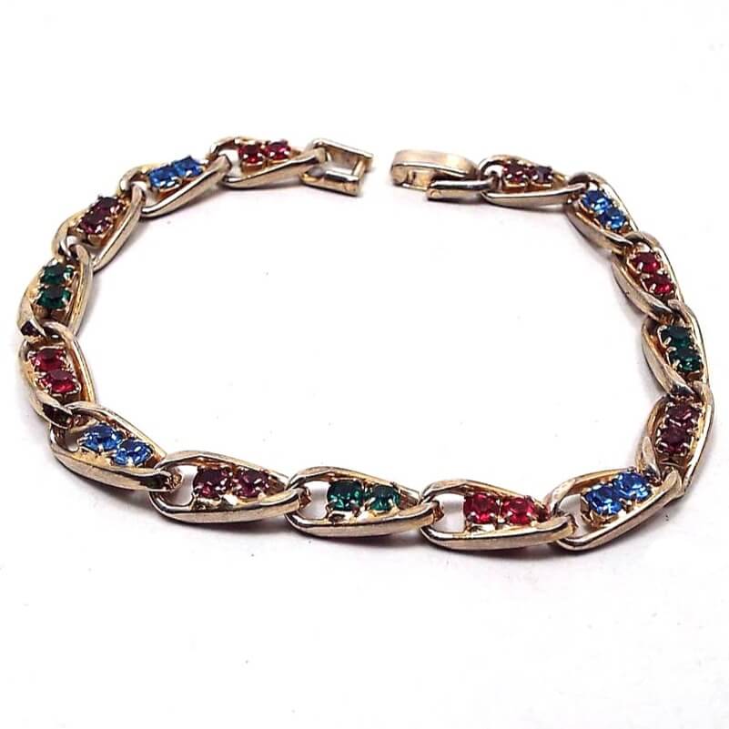 Top view of the Mid Century vintage rhinestone bracelet. The metal is gold tone in color. The links are twisted oval shape and each link has two rhinestones. The colors alternate between the links of red, blue, green, and purple rhinestones. 