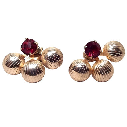 Front view of the Mid Century vintage Duane screw back earrings. They are gold tone in color. There are three round areas with lines on the bottoms that are spread out similar to a fan like design. At the top is a round prong set rhinestone in dark red.