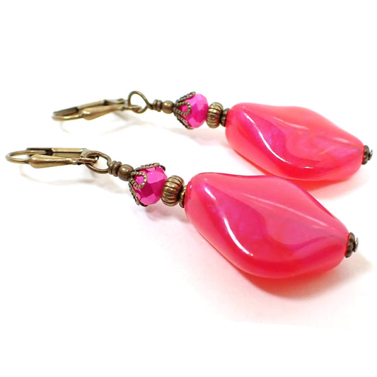 Angled side view of the handmade color shift earrings. The metal is antiqued brass in color. There are hot pink faceted glass crystals at the top. The bottom beads are shaped like curved and angled teardrops are are bright pink lucite with shimmers of purple color as you move around in the light.