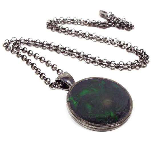 Front view of the handmade resin pendant. The metal is gunmetal plated dark gray. There is a rolo chain with a lobster claw clasp at the end. The round pendant has black and neon green swirls. 