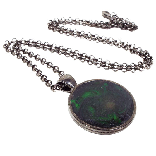 Front view of the handmade resin pendant. The metal is gunmetal plated dark gray. There is a rolo chain with a lobster claw clasp at the end. The round pendant has black and neon green swirls. 
