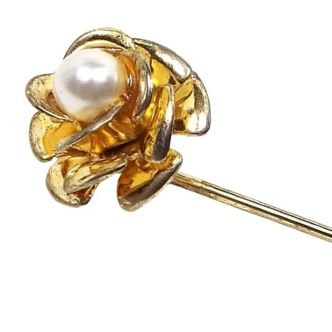 Enlarged view of the top of the Mid Century vintage faux pearl floral stick pin. The metal is gold tone in color. There is a flower design at the top with metal petals with an imitation pearl in the middle.