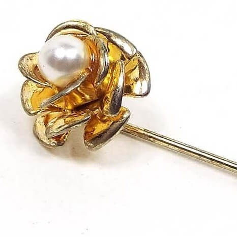 Enlarged view of the top of the Mid Century vintage faux pearl floral stick pin. The metal is gold tone in color. There is a flower design at the top with metal petals with an imitation pearl in the middle.