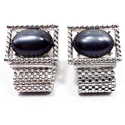 Front view of the Mid Century vintage Swank wrap around cufflinks. The metal and mesh link is silver tone in color. The tops are shaped like rectangles with large oval moonglow lucite cabs in the middle in a pearly dark gray color.