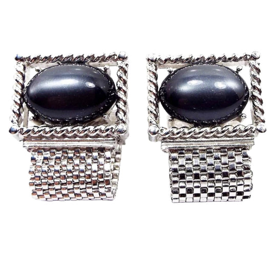 Front view of the Mid Century vintage Swank wrap around cufflinks. The metal and mesh link is silver tone in color. The tops are shaped like rectangles with large oval moonglow lucite cabs in the middle in a pearly dark gray color.