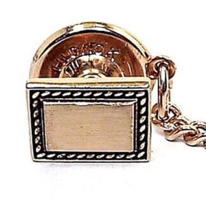 Front view of the Mid Century vintage rectangle Hickok tie tack. It is gold tone in color and has a black design around the edge.