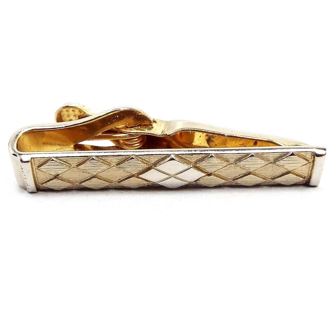 Front view of the Mid Century vintage small Swank tie clip. It is gold tone in color. The front has a diamond pattern design with textured matte gold tone color. The very middle has four diamond shapes making up a larger diamond shape and is shiny gold tone in color.