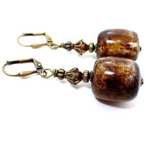 Side view of the chunky lucite handmade drop earrings. The metal is antiqued brass in color. There are brown faceted glass crystals at the top. The bottom beads are large barrel shaped and have shades of brown and off white. 
