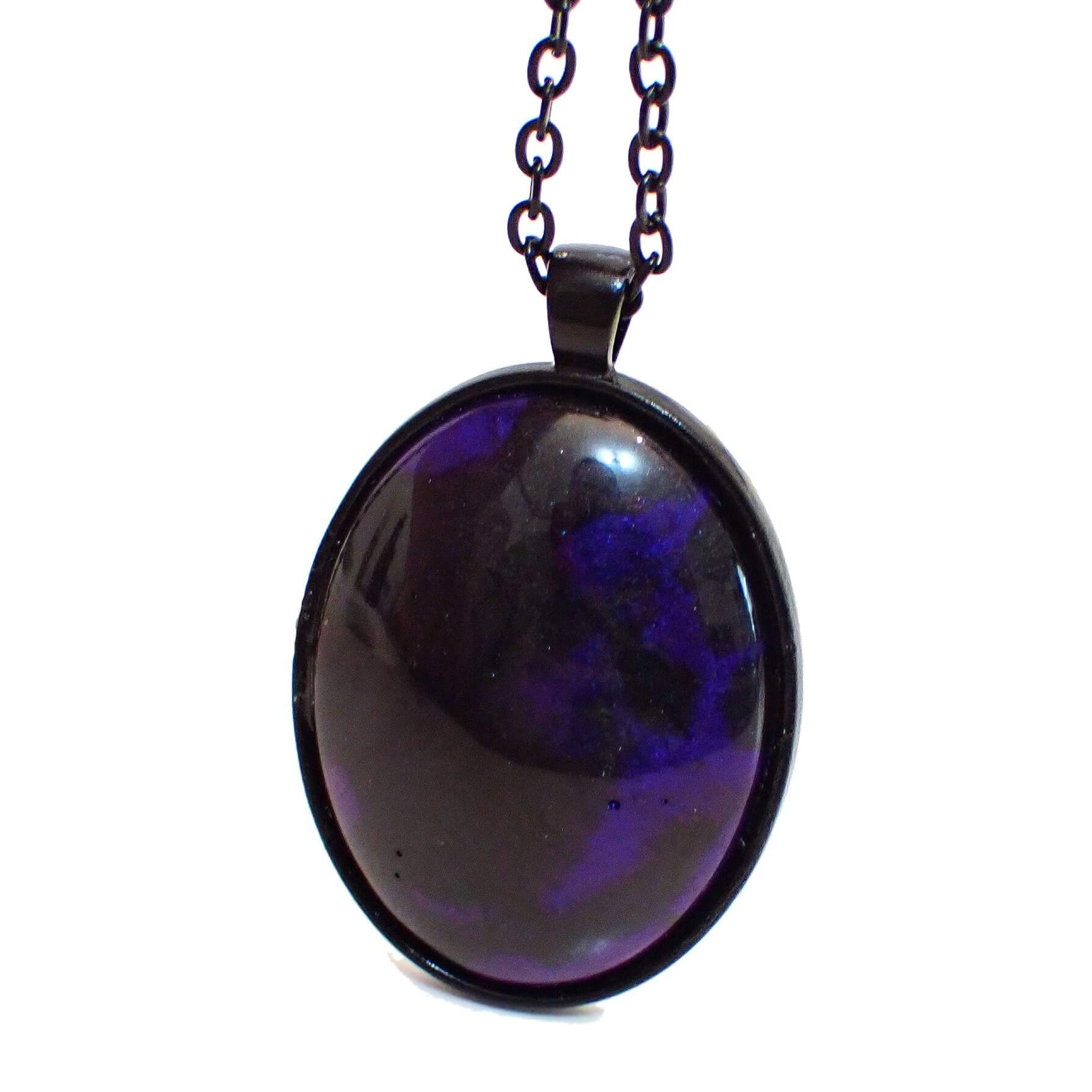 Enlarged front view of the handmade Goth resin pendant. The metal is black coated. There is a large domed oval pendant with pearly black and purple marbled resin. Some of the purple resin has hints of blue depending on how the light is hitting it.