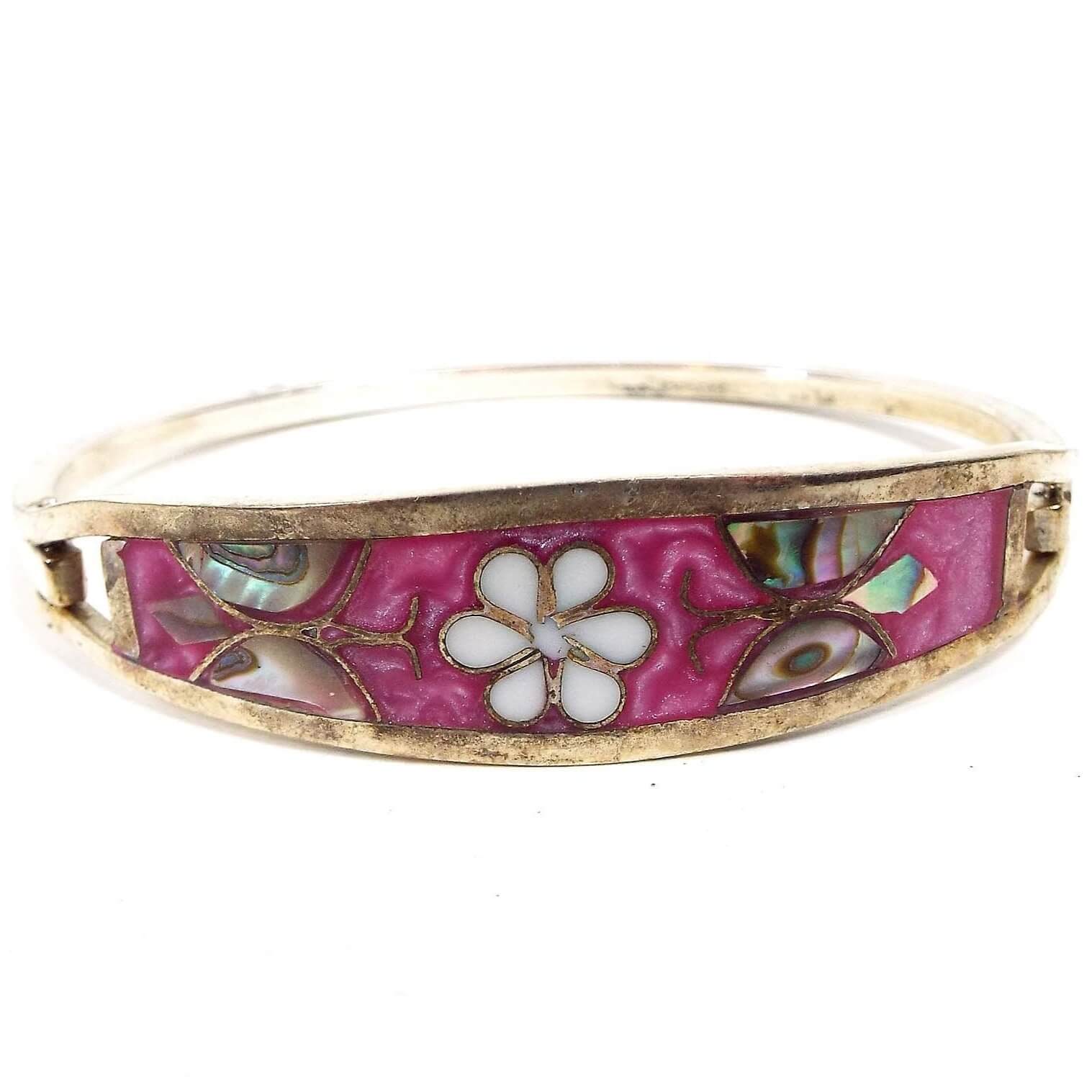 Front view of the retro vintage bangle bracelet with inlaid abalone. The front has a light pearly pink enamel with a white flower in the middle. On each side is a butterfly made of inlaid abalone shell. 