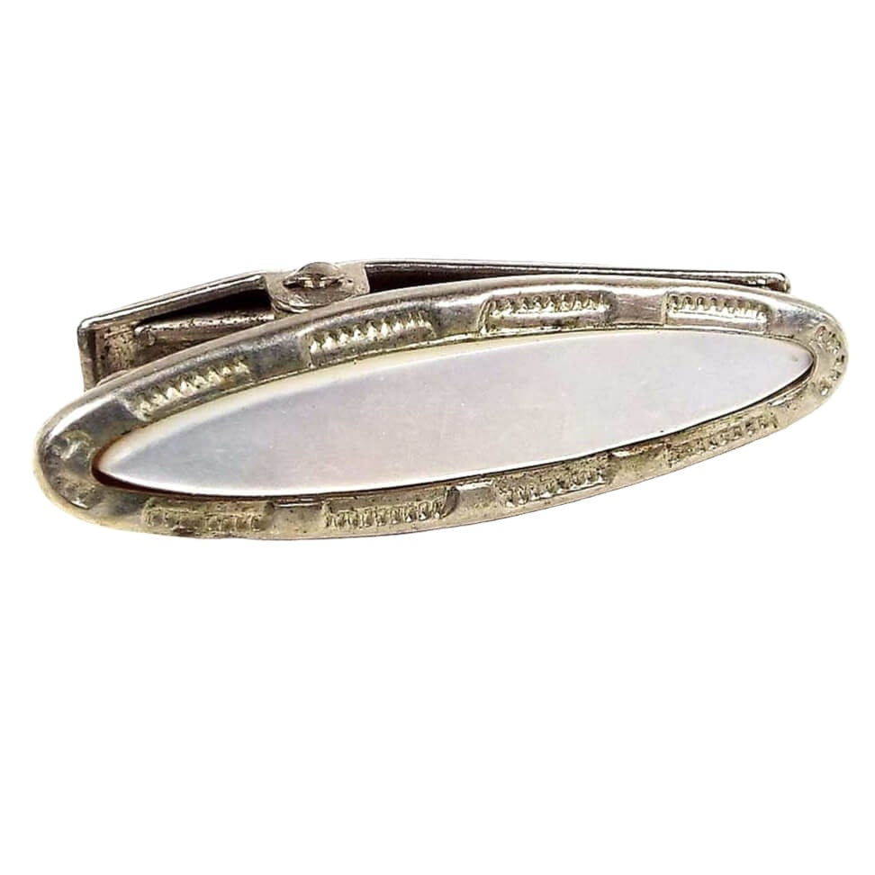 Front view of the small Mid Century vintage mother of pearl tie clip. It is oval in shape and the metal is silver tone in color. There is a stamped design around the edge and a mother of pearl shell cab on the front.