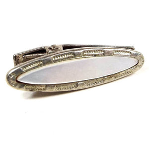 Front view of the small Mid Century vintage mother of pearl tie clip. It is oval in shape and the metal is silver tone in color. There is a stamped design around the edge and a mother of pearl shell cab on the front.
