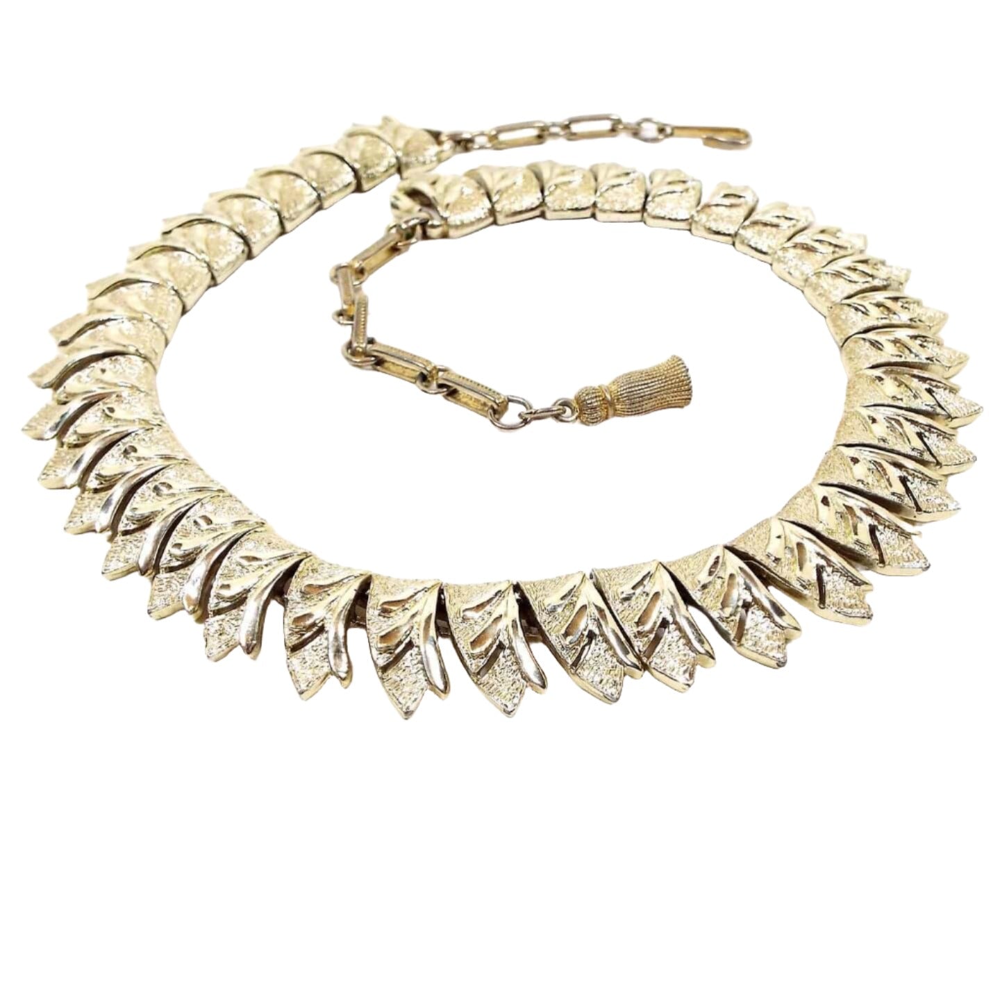 Front view of the Mid Century vintage Coro link choker necklace. It is gold tone in color. The links are shaped like ribbon ends and have an etched leaf type pattern cut on them. There is a hook clasp at the end.