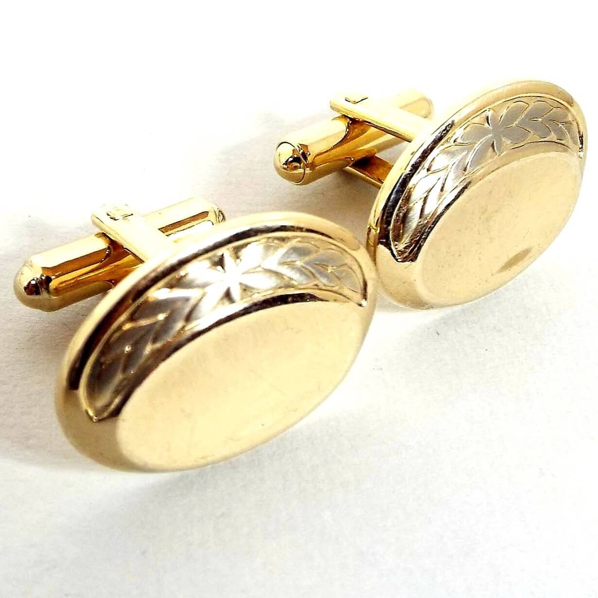 Angled front view of the retro vintage Hickok cufflinks. They are oval in shape and mostly gold tone in color. There is a silver tone leaf design around the top edge.