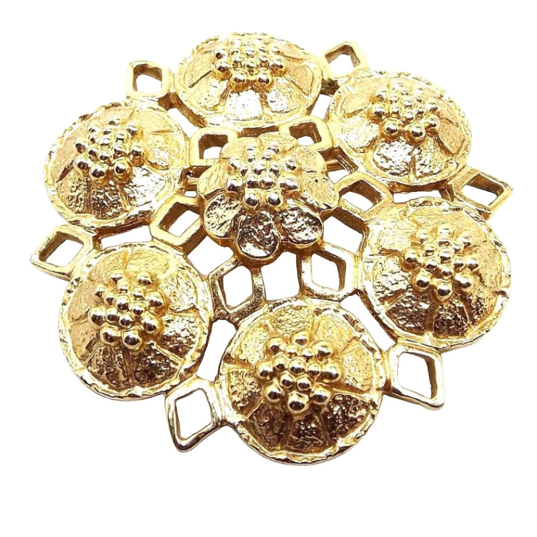 Front view of the Mid Century Vintage Sarah Coventry floral brooch pin. The metal is gold tone in color. The brooch has a filigree star shape with six round flower shapes around the outside of the brooch and a flower shape in the middle.