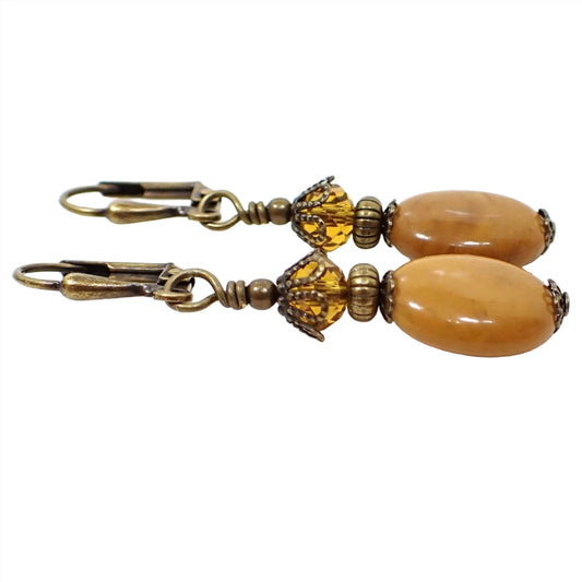 Side view of the handmade gemstone earrings. The metal is antiqued brass in color. There are faceted glass crystal beads at the top in a citrine orange color. The bottom jasper beads are oval shaped and have shades of mustard yellow, brown, and hints of orange.